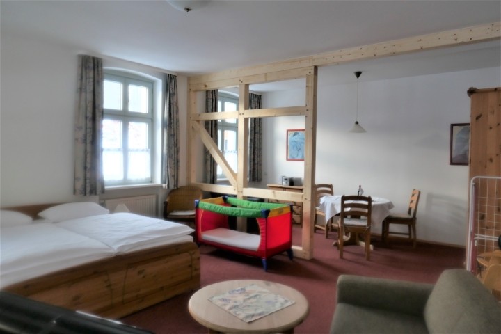 großer runder Tisch und Sessel, vorn Couch mit Tisch und TV