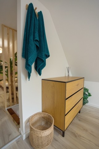 Eine stilvolle Holzkommode für Ihre Kleidung und ein geflochtener Wäschekorb für alles, was Sie verstauen müssen – praktisch und schön in dieser ruhigen Ecke des Schlafzimmers.