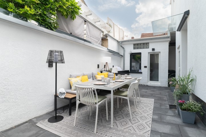 Terrasse (21 m²) im Hof: Außenküche mit elektrischem Grill und Spüle, viel Stauraum, Esstisch, Stühle und gepolsterte Sitzbank für 8 Personen, echte Topfpflanzen und Außenbeleuchtung – perfekt für gemeinsames Frühstück und entspannte Grillabende